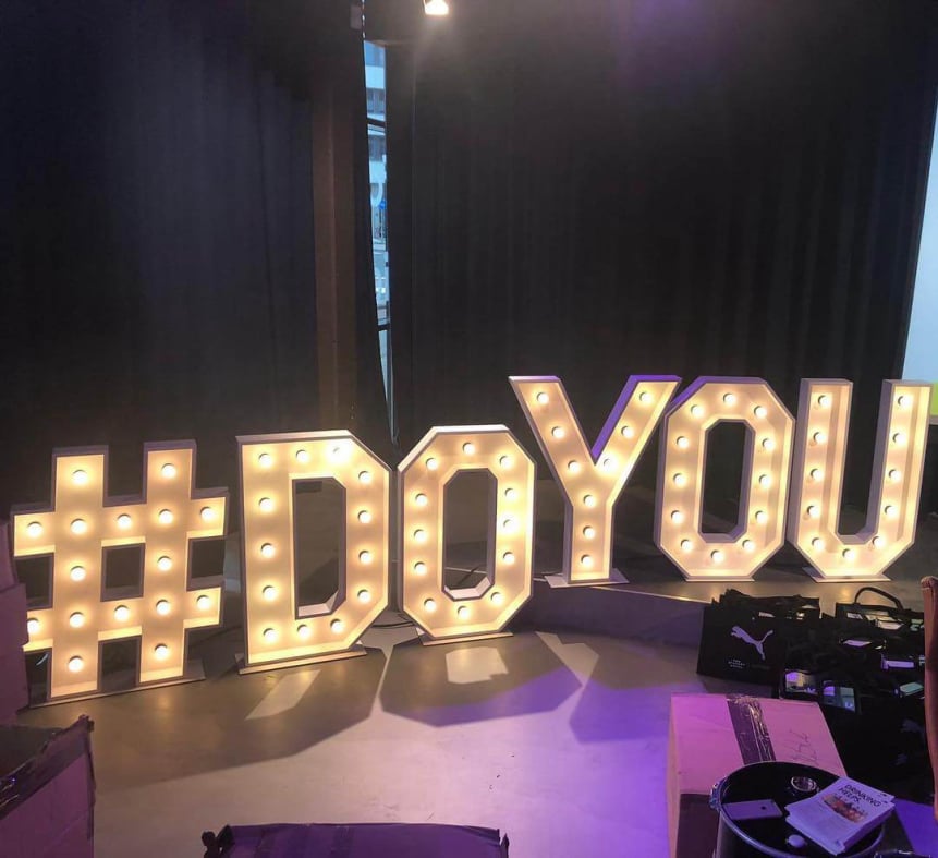 Vrouw op grote lichtletters buiten op de witte letters W en M