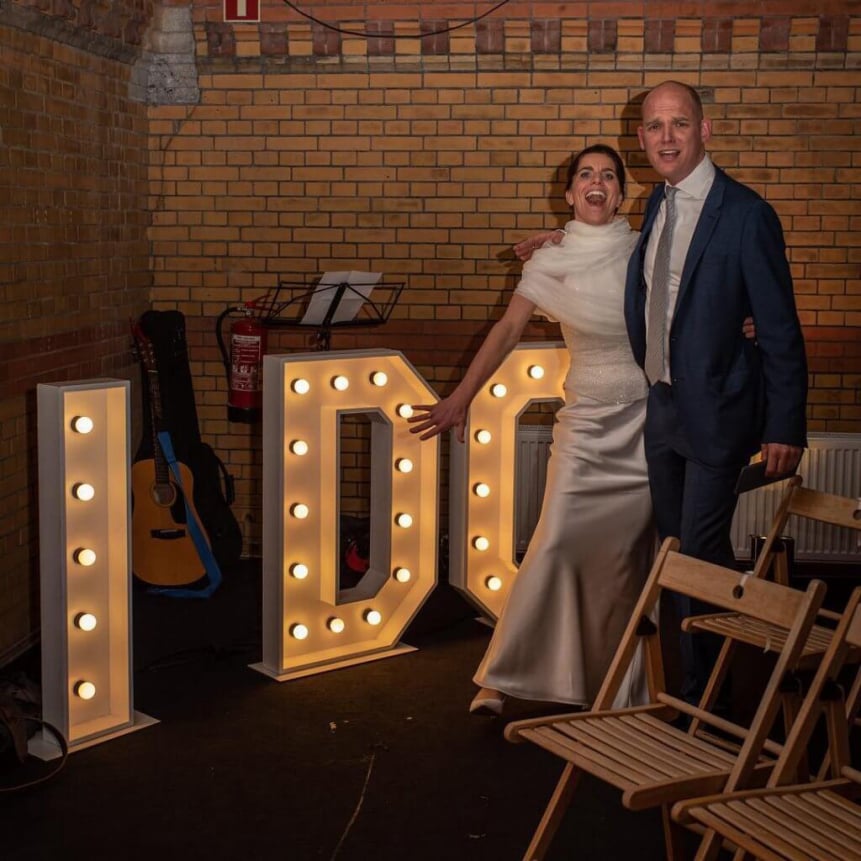 man en vrouw bij grote witte lichtletters ze krijgen korting op het huren van de photobooth